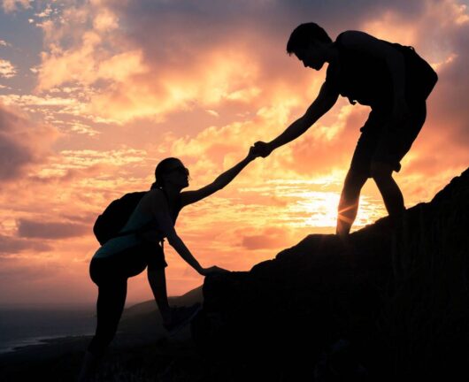 Team work. Man and woman helping each other climb up a mountain.